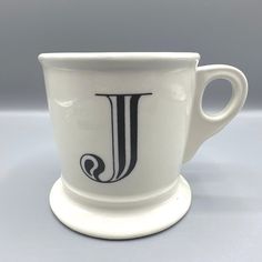 a white coffee cup with the letter j on it's side sitting on a saucer