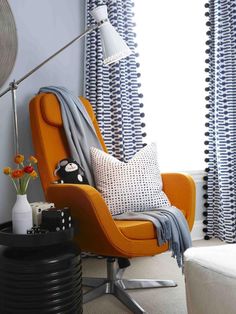 an orange chair in front of a window with black and white curtains