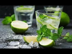 two glasses filled with ice and limes next to mint sprigs on a table