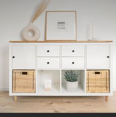 a white cabinet with wicker baskets on top and a plant in the corner next to it