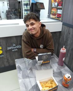 a man sitting at a table in front of a box of fries and a laptop