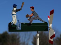 two figurines of baseball players on top of a green box with trees in the background