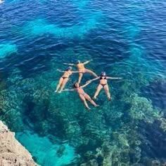 three people are swimming in the ocean with clear blue water and corals around them