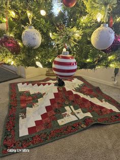 a christmas tree with ornaments hanging from it's branches and on top of the tree is a quilted table runner