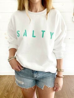 "The SALTY pullover sweatshirt is the perfect cozy top for breezy nights by the beach. Made from 50/50 cotton/poly blend, these unisex shirts are super soft and feature a ribbed waistband and cuffs. All text is hand painted using non-toxic fabric paint. The technique used creates an attractive distressed appearance to the text that varies slightly from shirt to shirt. All of my products are made to order. Production time usually takes between 3-5 business days from the time an order is placed. S White Long Sleeve Sweater For Beach Season, Beach Season Long Sleeve Letter Print Sweatshirt, Cotton Sweatshirt With Letter Print, Soft-washed Long Sleeve Sweatshirt For Summer, Soft-washed Long Sleeve Summer Sweatshirt, Long Sleeve Soft-washed Summer Sweatshirt, Summer Crew Neck Hoodie With Letter Print, Summer Letter Print Hoodie With Crew Neck, Relaxed Fit Cotton Beach Sweatshirt