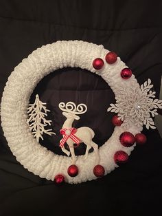 a white wreath with red ornaments and a reindeer on the front is surrounded by snowflakes