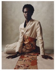 a man sitting on the ground in front of a rug wearing a white suit and tie