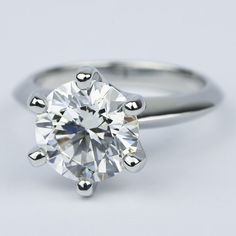 a round brilliant cut diamond ring on a plain surface, with the center stone set in 18k white gold