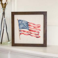 an american flag is displayed in a frame next to a vase with flowers and scissors