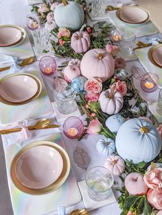 the table is set with pastel colored pumpkins, flowers and gold chargers on it