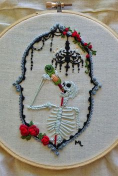 a cross stitched skeleton with flowers and a chandelier hanging from it's hoop