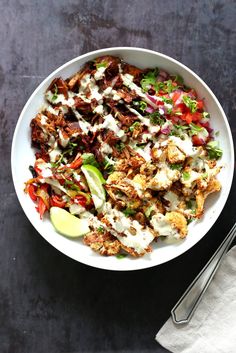 a white bowl filled with meat and veggies next to a fork on a table