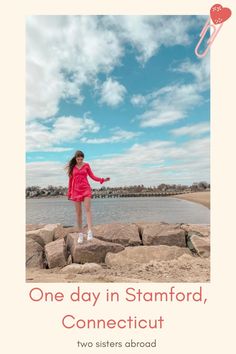 a girl in a pink dress is standing on rocks by the water with her arms outstretched