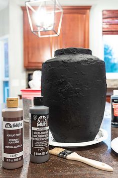 a large black cake sitting on top of a counter next to paint bottles and a brush