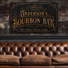 a brown leather couch in front of a brick wall with an old fashioned bourbon bar sign above it