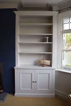 an empty white bookcase in front of a window with blue paint on the walls