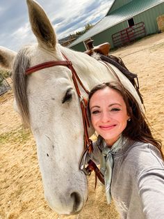 a woman standing next to a white horse on top of a dry grass covered field