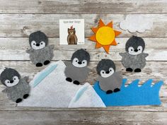 some felt animals sitting on top of a wooden table next to a book and an orange sun