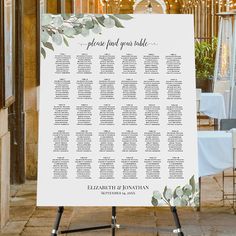 the seating chart for an outdoor wedding is displayed on a tripod with white linens and greenery