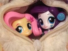 two little pony dolls are in the zipper of a white jacket with fur on it