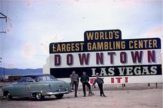 three men standing next to an old car in front of a sign for the world's largest gambling center down town las vegas