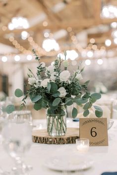 a vase with white flowers and greenery sits on a table at a wedding reception