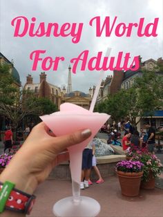 a hand holding up a pink drink in front of a fountain with people walking around