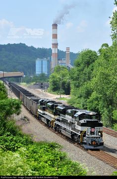 a train is traveling down the tracks in front of some smokestack stacks and trees