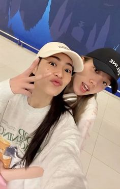 two girls are posing for the camera in front of a blue and white wall with an advertisement on it