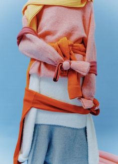 a doll is dressed in an orange and pink outfit, holding a yellow scarf over her head