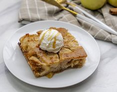 a piece of pie on a white plate with ice cream and apples in the background