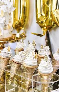 an assortment of ice cream cones on display in front of gold balloons and streamers