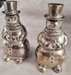 two silver snowmen sitting next to each other on a white tablecloth covered table