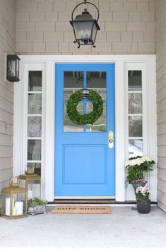 a blue front door with a wreath on it and two lanterns hanging from the side