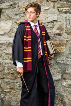 a young man dressed in harry potter robes and holding a wand while standing next to a stone wall