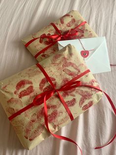 two wrapped presents with red ribbon on top of a white sheet covered in envelopes