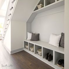 a white room with some shelves filled with shoes and baskets next to a stair case