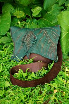 a green purse sitting on top of a lush green grass covered field next to leaves