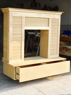 an unfinished wooden dog house with the door open and drawers closed in front of it