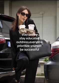 a woman in black holding a coffee cup and a tray with drinks on it, while standing next to a car