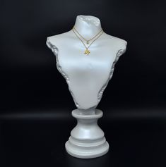 a white mannequin with a gold necklace on it's neck, against a black background