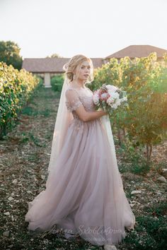 a woman in a wedding dress holding a bouquet and standing in front of an orchard