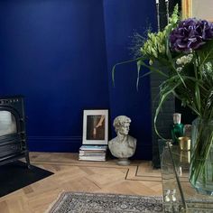 there is a vase with purple flowers on the floor next to a blue wall and an old fashioned stove