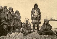 an old black and white photo of some people sitting on the ground with one person standing