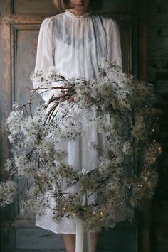 a woman standing in front of a door holding a wreath with flowers on the side