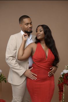 a woman in a red dress and a man in a beige suit stand next to each other