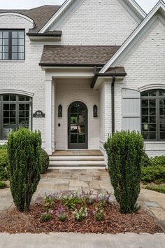 a white brick house with two front doors and some bushes in the front lawn area