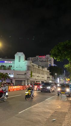 cars and motorcycles are driving down the street at night with buildings in the back ground