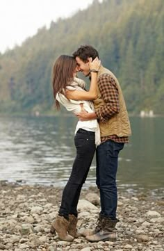 a man and woman kissing on the shore of a lake