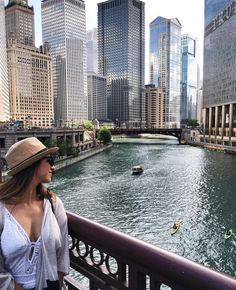 a woman is standing on a bridge looking at the river and boats in the water